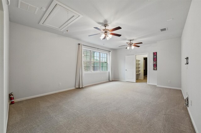 empty room featuring attic access, light colored carpet, a ceiling fan, and baseboards