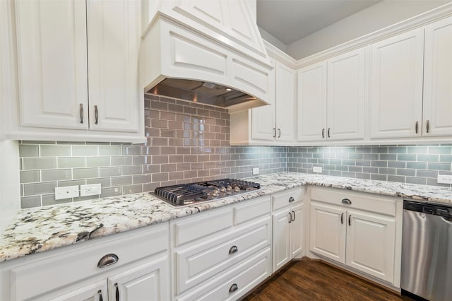 kitchen featuring stainless steel appliances, premium range hood, white cabinets, backsplash, and light stone countertops