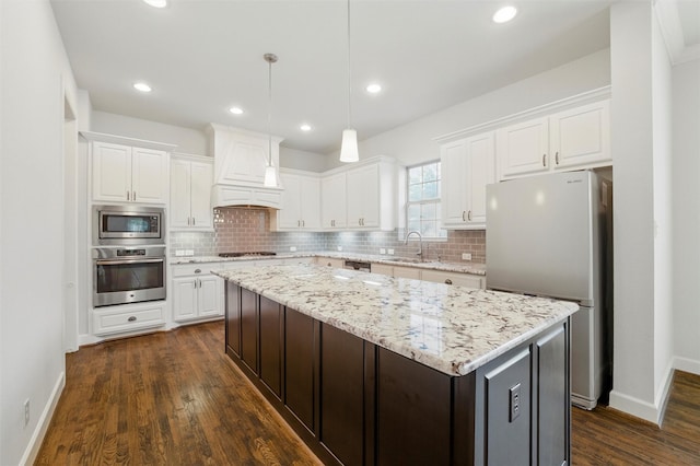 kitchen featuring appliances with stainless steel finishes, custom range hood, a sink, white cabinets, and a kitchen island