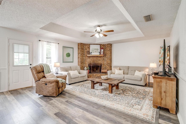 213 NE Timber Ridge Dr, Burleson, TX 76028 - living area with a textured ceiling, a raised ceiling, wood finished floors, a ceiling fan, and a fireplace