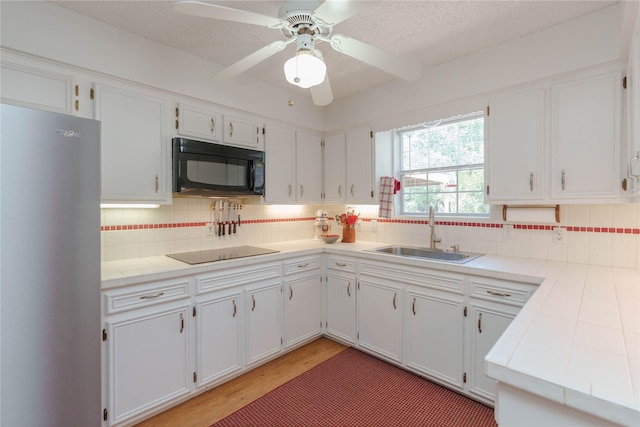 226 Highland Dr, Decatur, TX 76234 - kitchen featuring black appliances, a sink, white cabinets, light wood-type flooring, and a textured ceiling