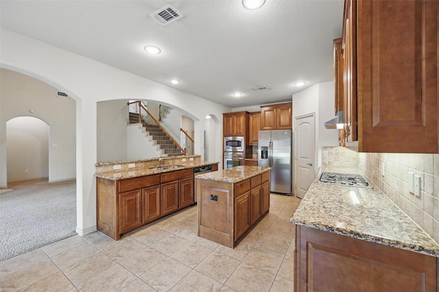 6824 San Fernando Dr, Fort Worth, TX 76131 - kitchen with stainless steel appliances, a sink, brown cabinets, light stone counters, and backsplash