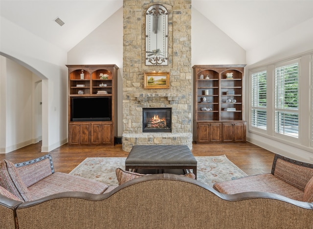living room with high vaulted ceiling, a fireplace, wood finished floors, arched walkways, and baseboards