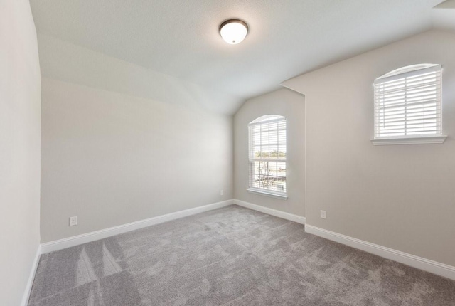 carpeted spare room with lofted ceiling and baseboards