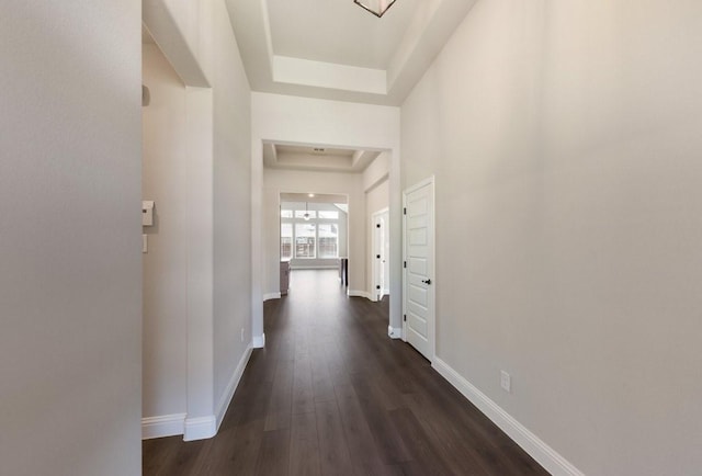 corridor featuring dark wood-style flooring, a raised ceiling, and baseboards