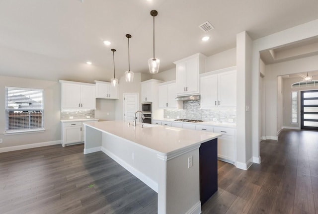 kitchen featuring gas stovetop, under cabinet range hood, backsplash, a large island, and dark wood-style flooring