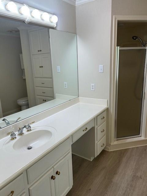 301 Village Cir, Waco, TX 76710 - full bathroom featuring wood finished floors, a shower stall, ornamental molding, vanity, and toilet