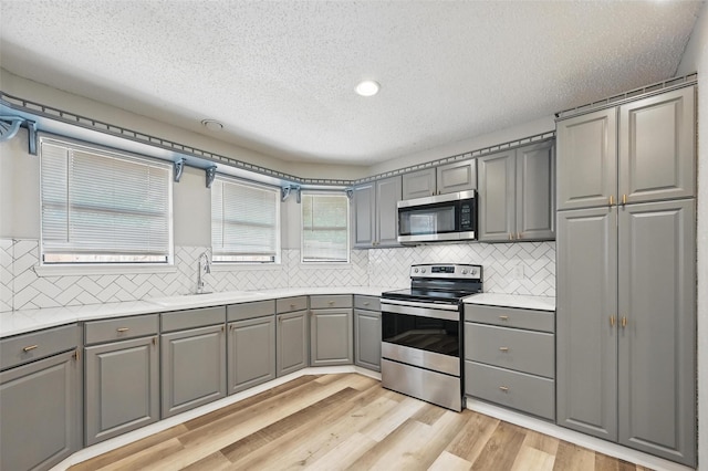 8805 Wood Glen Dr, Rowlett, TX 75088 - kitchen featuring stainless steel appliances, gray cabinetry, a sink, a textured ceiling, and light wood-style flooring