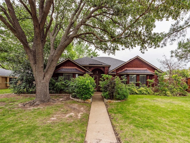 english style home featuring a front yard, roof with shingles, and brick siding