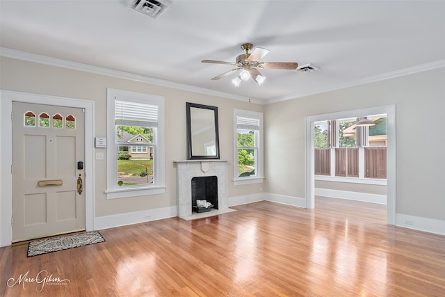 unfurnished living room with plenty of natural light, ceiling fan, light wood-type flooring, a fireplace with flush hearth, and ornamental molding