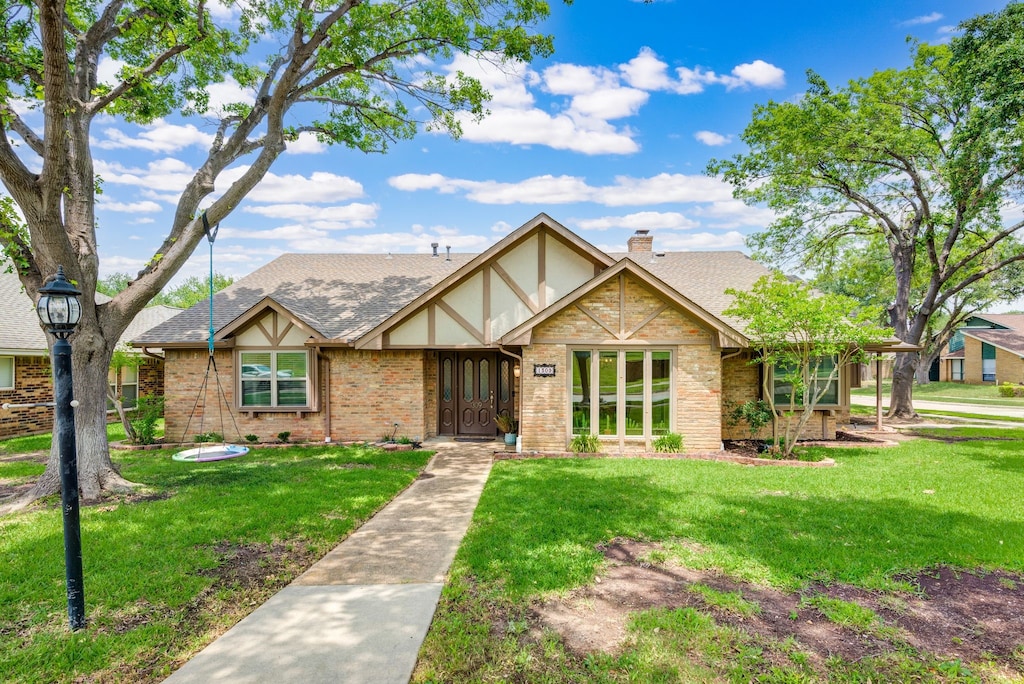 1309 Tierra Calle, Carrollton, TX 75006 - english style home featuring a front yard, brick siding, a chimney, and roof with shingles