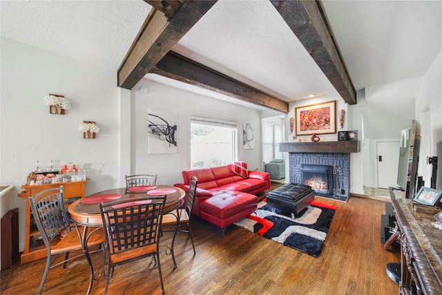 dining room with beamed ceiling, wood finished floors, a fireplace, and a textured ceiling