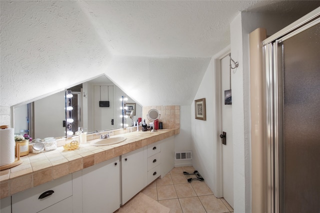 full bath featuring a textured ceiling, vaulted ceiling, vanity, a shower with shower door, and tile patterned floors