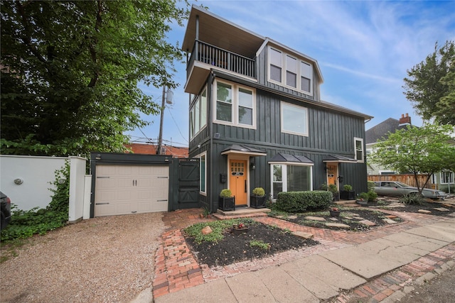 view of front facade featuring a balcony, board and batten siding, driveway, an attached garage, and a gate
