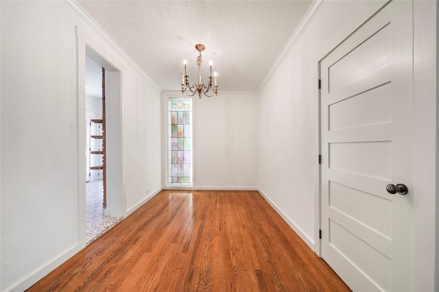 spare room featuring crown molding, a chandelier, wood finished floors, and baseboards