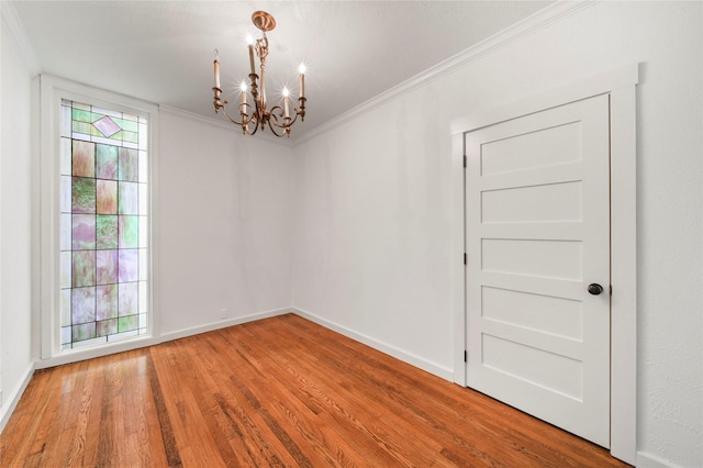 empty room with a chandelier, wood finished floors, ornamental molding, and baseboards