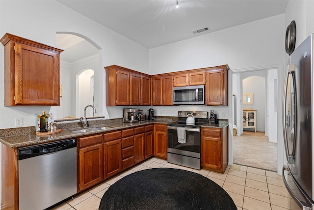 221 Whitestone Way, Weatherford, TX 76085 - kitchen with stainless steel appliances, a sink, light tile patterned floors, arched walkways, and brown cabinetry