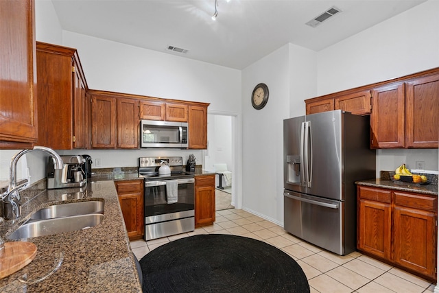 221 Whitestone Way, Weatherford, TX 76085 - kitchen featuring appliances with stainless steel finishes, a sink, light tile patterned floors, dark stone countertops, and brown cabinetry