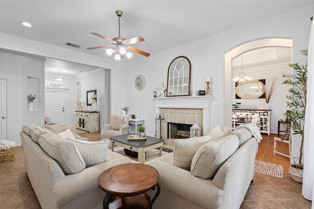 221 Whitestone Way, Weatherford, TX 76085 - living room featuring tile patterned flooring, a tile fireplace, a ceiling fan, crown molding, and a chandelier