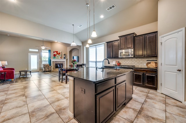 2617 Castle Creek Dr, Little Elm, TX 75068 - kitchen featuring stainless steel microwave, vaulted ceiling, a glass covered fireplace, open floor plan, and healthy amount of natural light