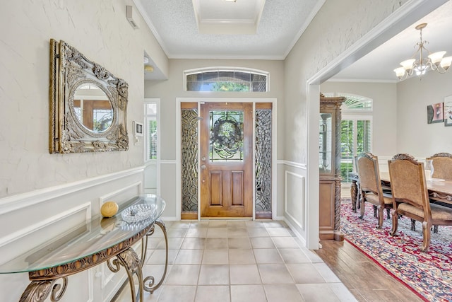 entrance foyer with ornamental molding, plenty of natural light, a textured ceiling, a chandelier, and a decorative wall
