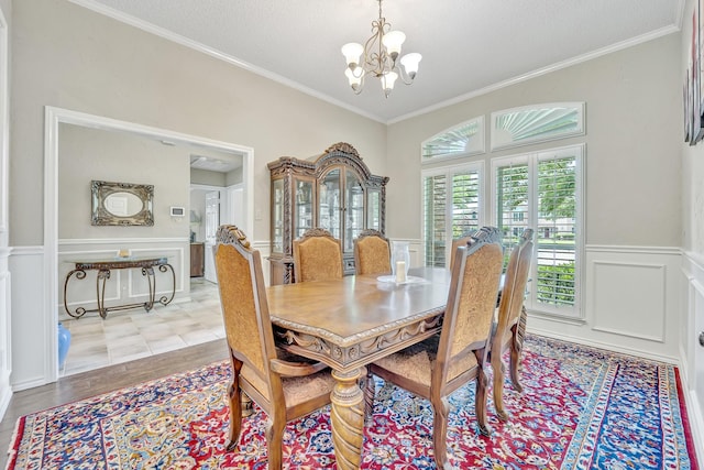 dining area with a chandelier, crown molding, a wainscoted wall, a decorative wall, and a textured ceiling