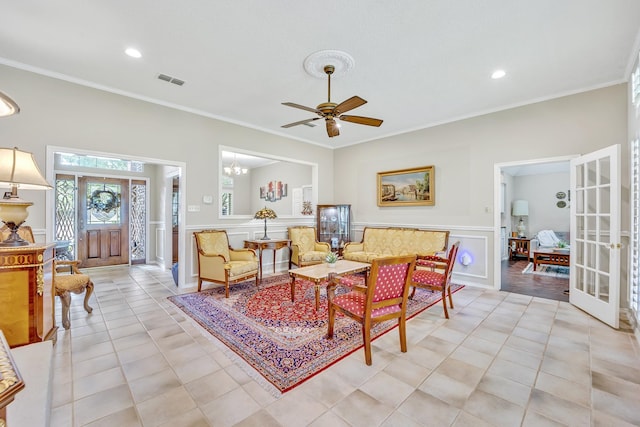 living area featuring ceiling fan, french doors, ornamental molding, a wainscoted wall, and light tile patterned floors