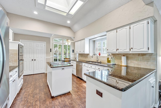 kitchen featuring a sink, appliances with stainless steel finishes, a center island, vaulted ceiling, and dark wood finished floors