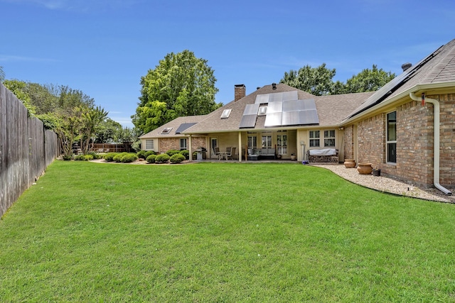 back of house with a chimney, brick siding, solar panels, and a patio