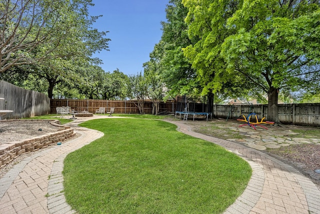 view of yard featuring a trampoline, a fire pit, and a patio