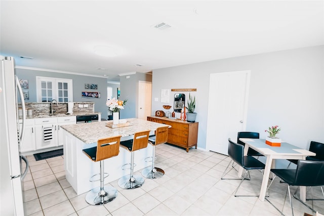 1433 Sun Breeze Dr, Little Elm, TX 75068 - kitchen featuring freestanding refrigerator, a center island, a kitchen breakfast bar, white cabinetry, and light stone counters