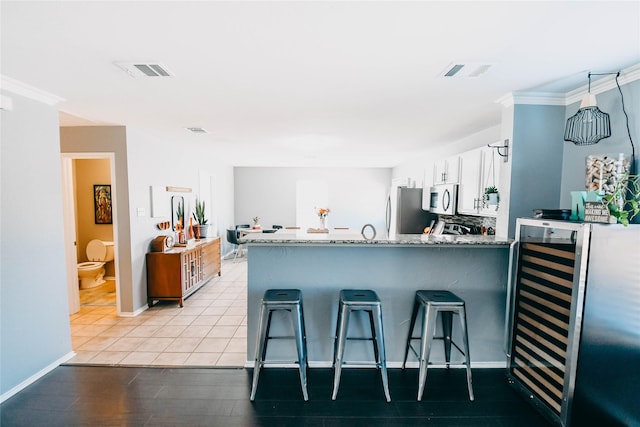 1433 Sun Breeze Dr, Little Elm, TX 75068 - kitchen with appliances with stainless steel finishes, a peninsula, white cabinets, a kitchen breakfast bar, and light stone counters