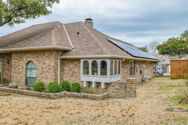 10014 Silver Creek Rd, Dallas, TX 75243 - view of home's exterior with brick siding, solar panels, a chimney, roof with shingles, and a yard