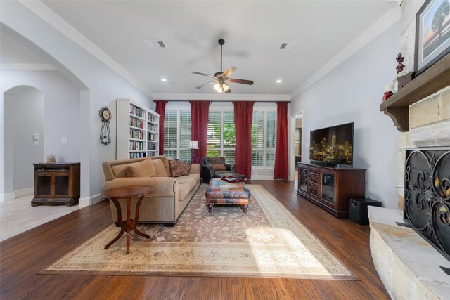 8803 Kelvington Dr, Frisco, TX 75035 - living room featuring a fireplace with raised hearth, crown molding, arched walkways, ceiling fan, and wood finished floors