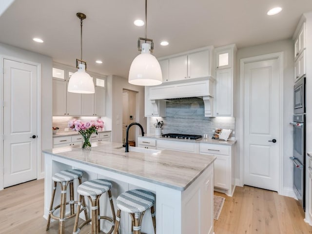 4837 Cumberland Cir, Carrollton, TX 75010 - kitchen featuring a sink, a kitchen island with sink, light wood-style flooring, backsplash, and recessed lighting