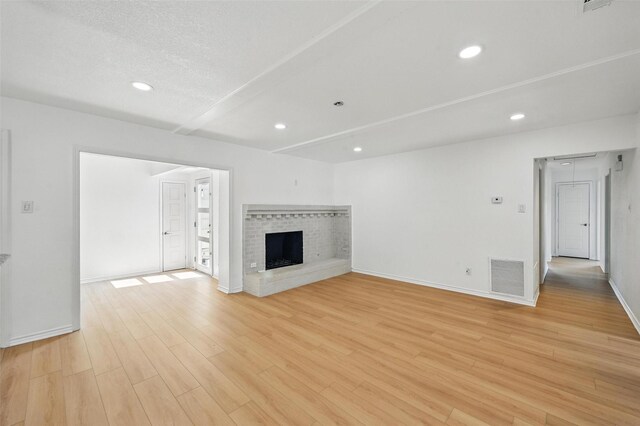 700 Brentwood Ln, Richardson, TX 75080 - unfurnished living room featuring light wood-style flooring, baseboards, a brick fireplace, recessed lighting, and a textured ceiling