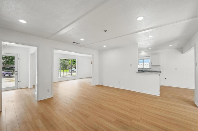 700 Brentwood Ln, Richardson, TX 75080 - unfurnished living room featuring a textured ceiling, baseboards, light wood-style flooring, recessed lighting, and a sink