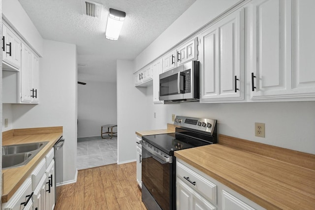 4448 Wind River Ln, Garland, TX 75042 - kitchen with appliances with stainless steel finishes, white cabinets, a sink, light wood-style floors, and a textured ceiling