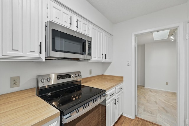 4448 Wind River Ln, Garland, TX 75042 - kitchen featuring appliances with stainless steel finishes, white cabinets, a skylight, and baseboards