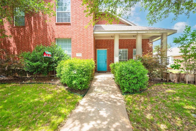entrance to property with brick siding and a yard