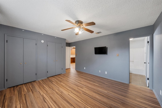 178 Norwood Dr, Woodway, TX 76712 - unfurnished bedroom featuring wood finished floors, two closets, a textured ceiling, ensuite bathroom, and baseboards