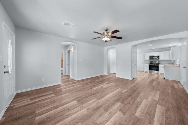 804 Hemlock Dr, West Tawakoni, TX 75474 - unfurnished living room featuring a ceiling fan, arched walkways, light wood-style floors, and baseboards