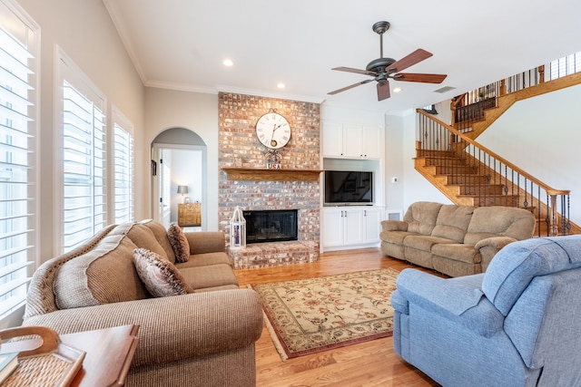 112 Mustang Dr, Fate, TX 75087 - living room with a ceiling fan, light wood-type flooring, ornamental molding, arched walkways, and a brick fireplace