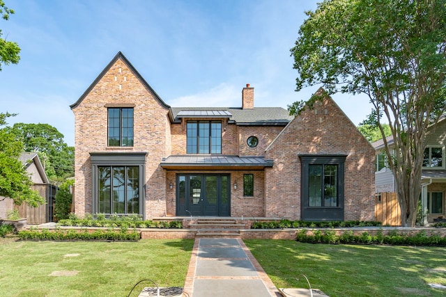 9715 Shadydale Ln, Dallas, TX 75238 - tudor-style house featuring brick siding, a front yard, a chimney, a standing seam roof, and french doors