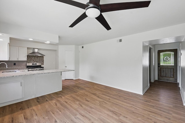 kitchen featuring stainless steel range with gas cooktop, a sink, wall chimney range hood, light wood-style floors, and recessed lighting
