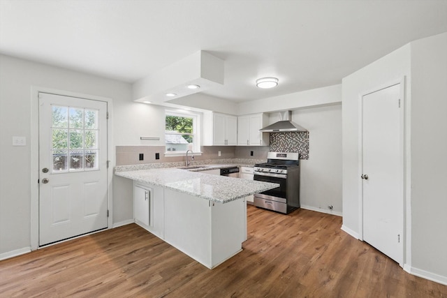 kitchen featuring stainless steel appliances, a sink, a peninsula, wall chimney range hood, and white cabinets