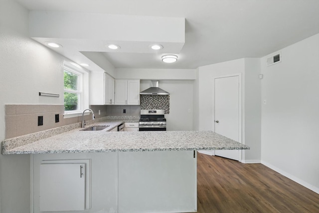 kitchen with stainless steel gas stove, a sink, wall chimney range hood, a peninsula, and backsplash