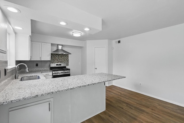 kitchen featuring stainless steel gas range, wall chimney range hood, a sink, a peninsula, and baseboards