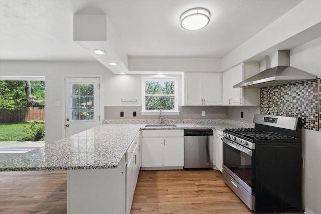 kitchen with appliances with stainless steel finishes, wall chimney exhaust hood, a sink, a peninsula, and plenty of natural light