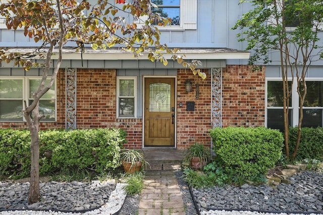 view of exterior entry with brick siding, cooling unit, and board and batten siding